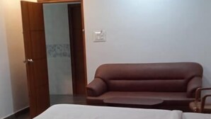 A bedroom with a bed, a brown sofa, and a wooden door. - J Residency (Pochampalli)