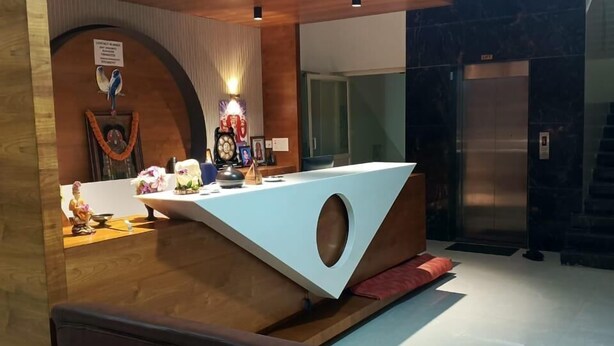 A modern reception area with a wooden reception desk, a blue sofa, and a decorative wall with a bird and a clock. - J Residency (Pochampalli)
