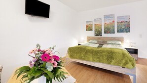 A bedroom with a bed, a flat-screen TV, and three wall-mounted paintings. - Holiday Apartment Am Wiesenweg with Private Terrace and Wi-Fi (Mauerstetten)