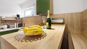 A kitchen with a wooden countertop, a fruit bowl with bananas, a bottle of champagne, and a microwave. - Holiday Apartment Am Wiesenweg with Private Terrace and Wi-Fi (Mauerstetten)