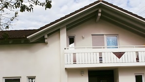 A two-story building with a balcony, a driveway, and a small garden area. - Holiday Apartment Am Wiesenweg with Private Terrace and Wi-Fi (Mauerstetten)