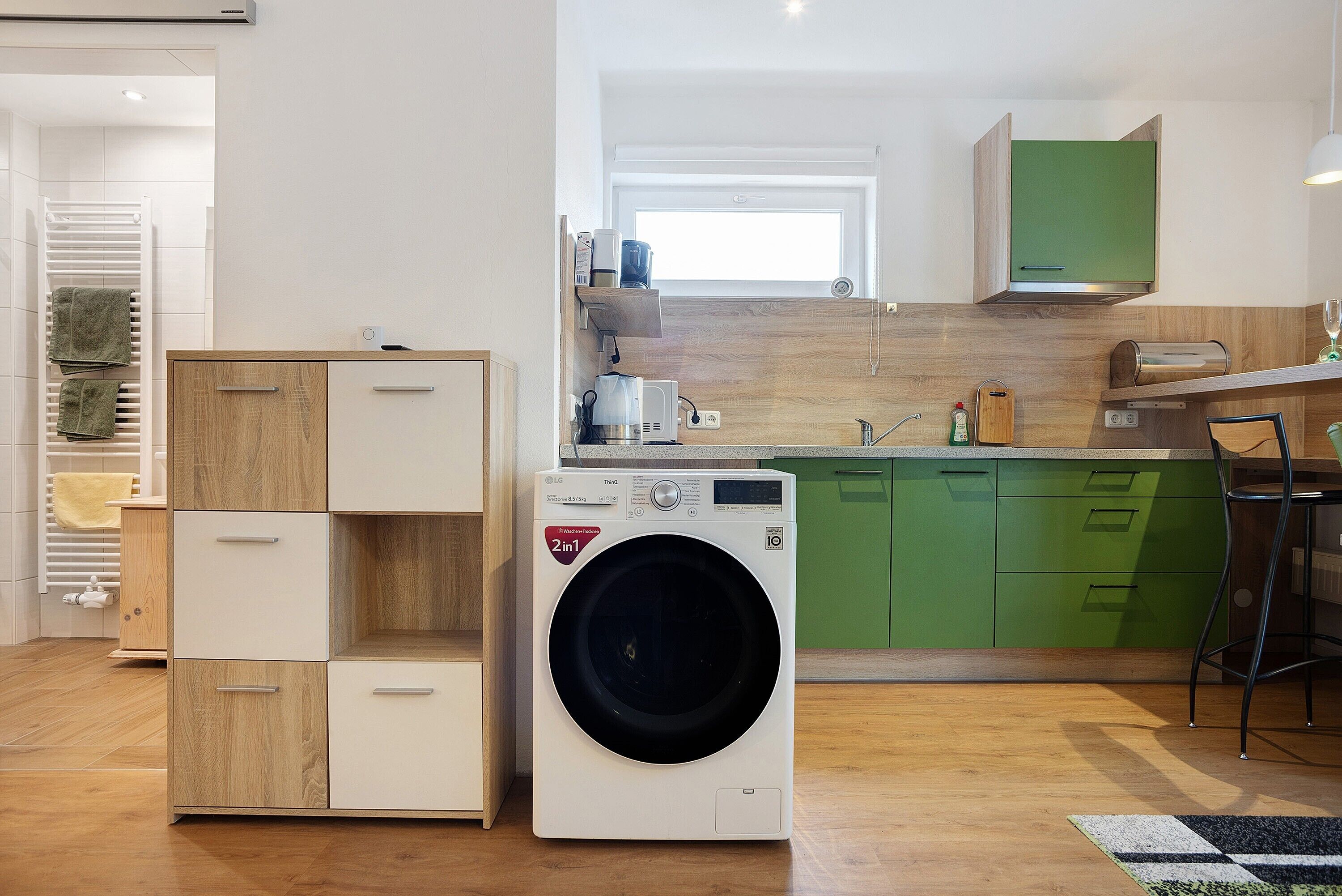 Uma cozinha compacta com máquina de lavar, armários de madeira e bancada verde.