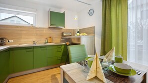 A modern kitchen with green cabinets, a wooden dining table, and a window with a view of a house. - Holiday Apartment Am Wiesenweg with Private Terrace and Wi-Fi (Mauerstetten)