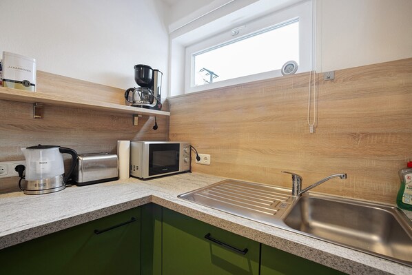 A kitchen with a microwave, toaster, coffee maker, and a sink.