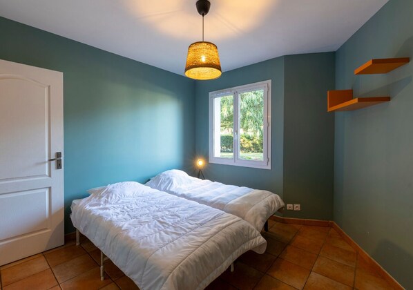 A bedroom with two beds, a window, and a hanging light fixture.
