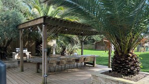 Een houten terras met een pergola, zitplaatsen buiten en een palmboom.