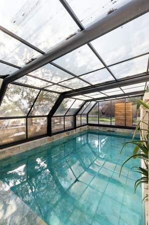 A swimming pool with a glass ceiling, surrounded by stone walls and a wooden deck.