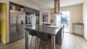 Een moderne keuken met een centraal eiland, roestvrijstalen apparatuur en uitzicht naar buiten.