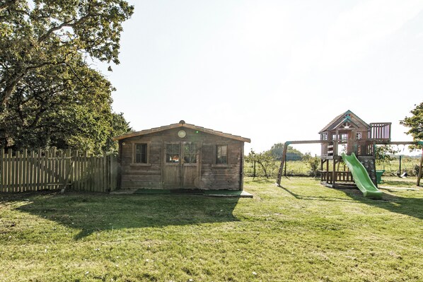 A wooden cabin with a green slide and a wooden deck.