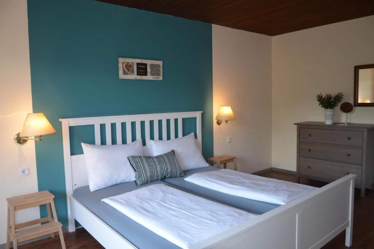 A bedroom with a bed, bedside tables, a dresser, and a wall-mounted light fixture.
