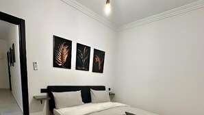 Un dormitorio moderno con una cama grande, paredes blancas y tres obras de arte colgadas.