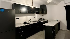 Cocina moderna con armarios negros, encimera blanca y una lámpara colgante.