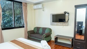 A hotel room with a bed, a green and brown sofa, a TV mounted on the wall, and a wooden floor. - Yangchhen Peace Home Bed & Breakfast (Kathmandu)