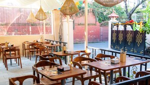 An indoor dining area with wooden tables and chairs, hanging wicker lamps, and a view of a red brick wall and greenery outside. - Yangchhen Peace Home Bed & Breakfast (Kathmandu)