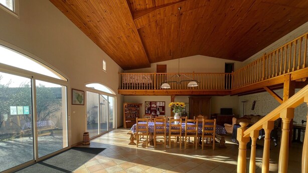A spacious interior with a high ceiling, a dining area with a table and chairs, a staircase, and a view through large glass doors. - Bed and Breakfast 'Chambre Mansardée' with Shared Terrace, Shared Garden and Wi-Fi (VERRIERES)