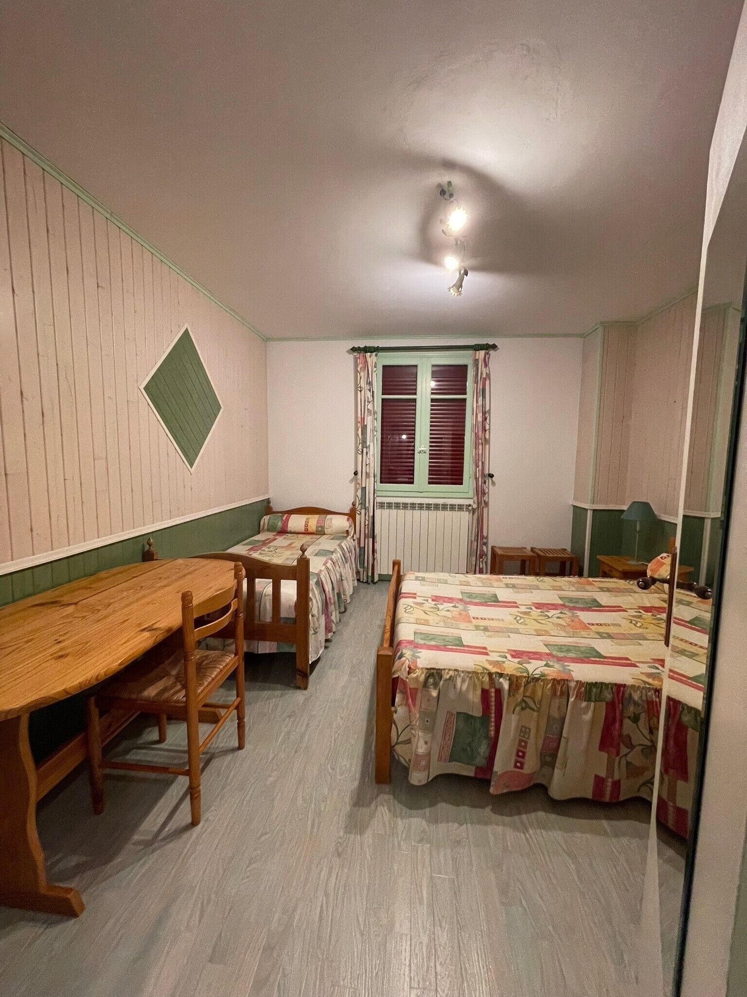 A room with two beds, a wooden table, and a radiator.