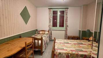 A room with two beds, a wooden table, and a radiator.