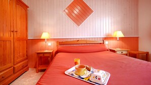 A hotel room with a wooden wardrobe, a bed with a red bedspread, two bedside tables with lamps, and a tray with a mug and a pastry. - Bed and Breakfast 'Chambre Saumon' with Shared Terrace, Shared Garden and Wi-Fi (VERRIERES)