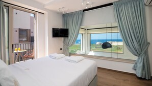 Une chambre d’hôtel avec un lit, une télévision, un balcon avec une table et des chaises, et une vue sur la mer.