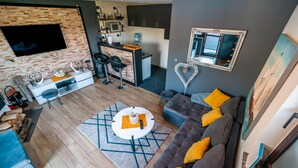 A modern living room with a grey sofa, a coffee table, and a TV mounted on a brick wall. - Gorgeous home in Slavonski Brod with sauna (Slavonski Brod)