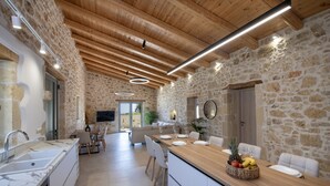 A modern kitchen with a stone wall, wooden ceiling, and a central island with fruit and glasses. - Fabrica Villa, By Hellocrete (Roupes)