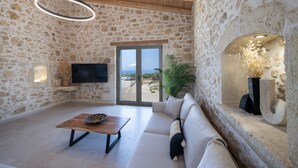 A stone-walled room with a wooden ceiling, a sofa, a coffee table, and a TV mounted on the wall. - Fabrica Villa, By Hellocrete (Roupes)