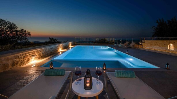 An infinity pool with a sunset view, a table with glasses and a bottle, and a lantern. - Fabrica Villa, By Hellocrete (Roupes)