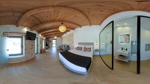 A modern hotel room with a curved bed, stone walls, wooden ceiling, and a glass-enclosed bathroom. - Fabrica Villa, By Hellocrete (Roupes)