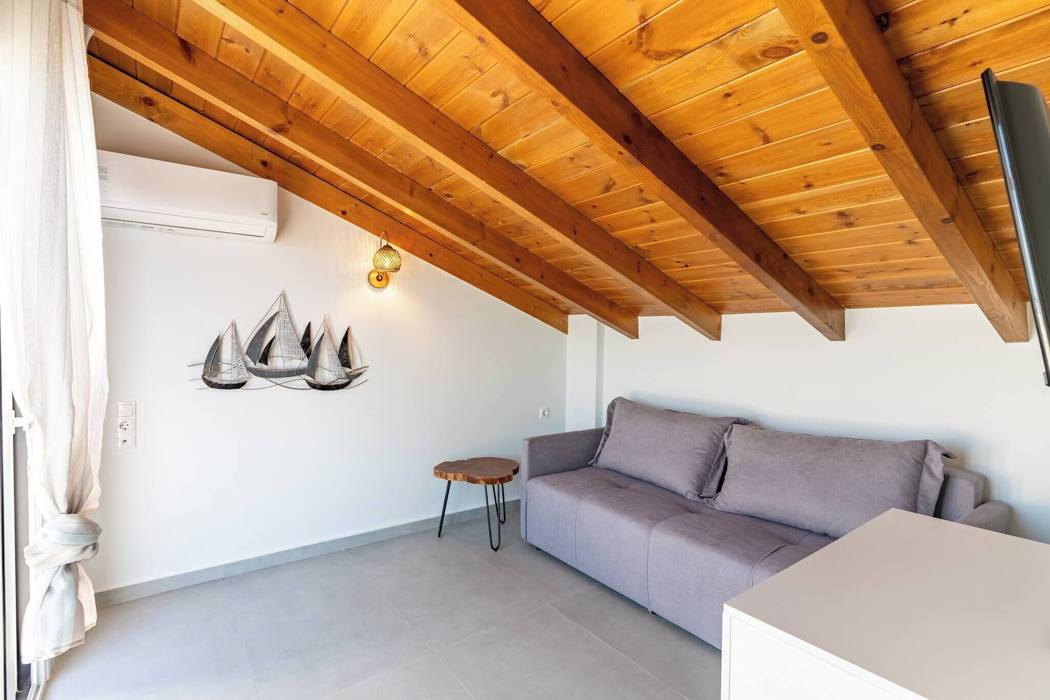 A room with a wooden ceiling, a gray sofa, a small round table, and wall-mounted decorative items.