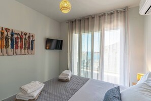 A hotel room with a bed, a TV mounted on the wall, a painting, and a window with curtains. - Lyra Suite (Panormo)
