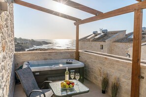 A balcony with a hot tub, table with fruits and wine glasses, and a view of the sea and buildings. - Armonia Suite (Panormo)