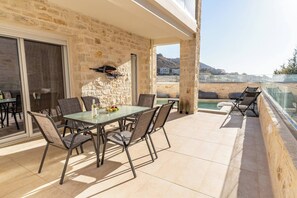 A terrace with a table and chairs, a stone wall, and a view of the landscape. - Armonia Suite (Panormo)