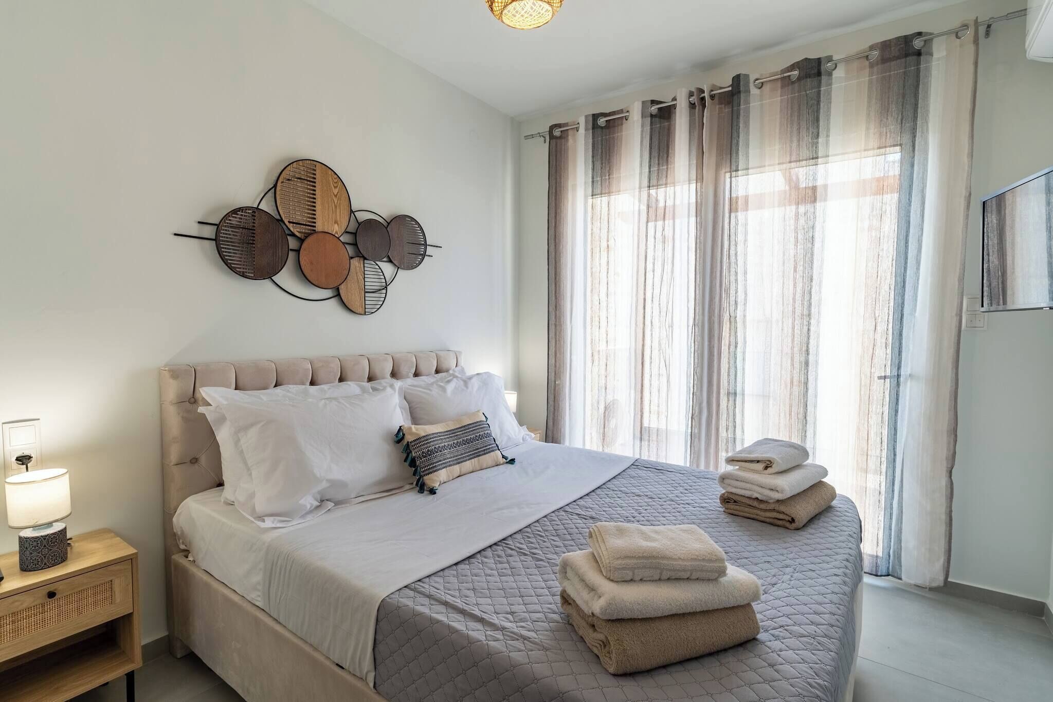 Ein ordentlich eingerichtetes Schlafzimmer mit einem Bett, Nachttischen, einem Wandbild und einem Fenster mit Vorhängen.