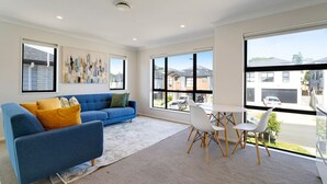 Un salon moderne avec un canapé bleu, une table blanche et des chaises, de grandes fenêtres et des œuvres d’art accrochées aux murs.