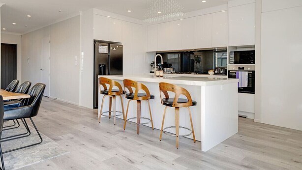 Une cuisine moderne avec des meubles blancs, un îlot central doté de tabourets, des appareils en acier inoxydable et un coin repas avec une table et des chaises.