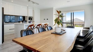 Une cuisine moderne avec des meubles blancs, une table à manger en bois et une grande fenêtre donnant sur l’extérieur.