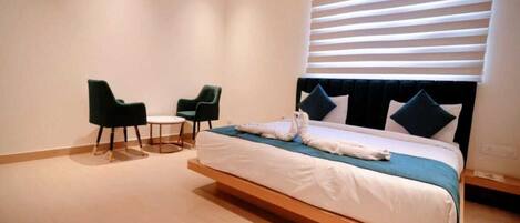 A modern hotel room with a large bed, two chairs, and a small table.