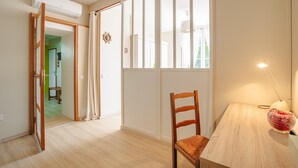 A room with a wooden floor, a dining table with a chair, a lamp, and a window with curtains. - Guest Room “Aix” – Spacious Family Suite in Aix (Virson)
