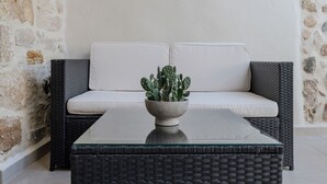A wicker sofa with a cushion, a table with a potted cactus, and a stone wall. - Stone Project 2 a cozy retreat with private Pool (Pigi)