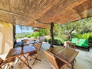An outdoor patio with wooden tables and chairs, a woven canopy, and a view of the countryside. - Grande Baglio Anastè by Interhome (Buseto Palizzolo)