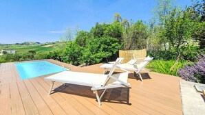 En træterrasse med pool, liggestole og udsigt over et grønt landskab.