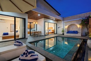 A modern hotel room with a large glass door, a pool, and a dining area with a table and chairs. - Diwangkara Villa Pandawa (Kutuh)