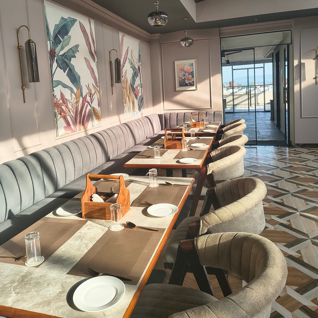 A restaurant with a long counter, cushioned seating, and a view through the glass doors.
