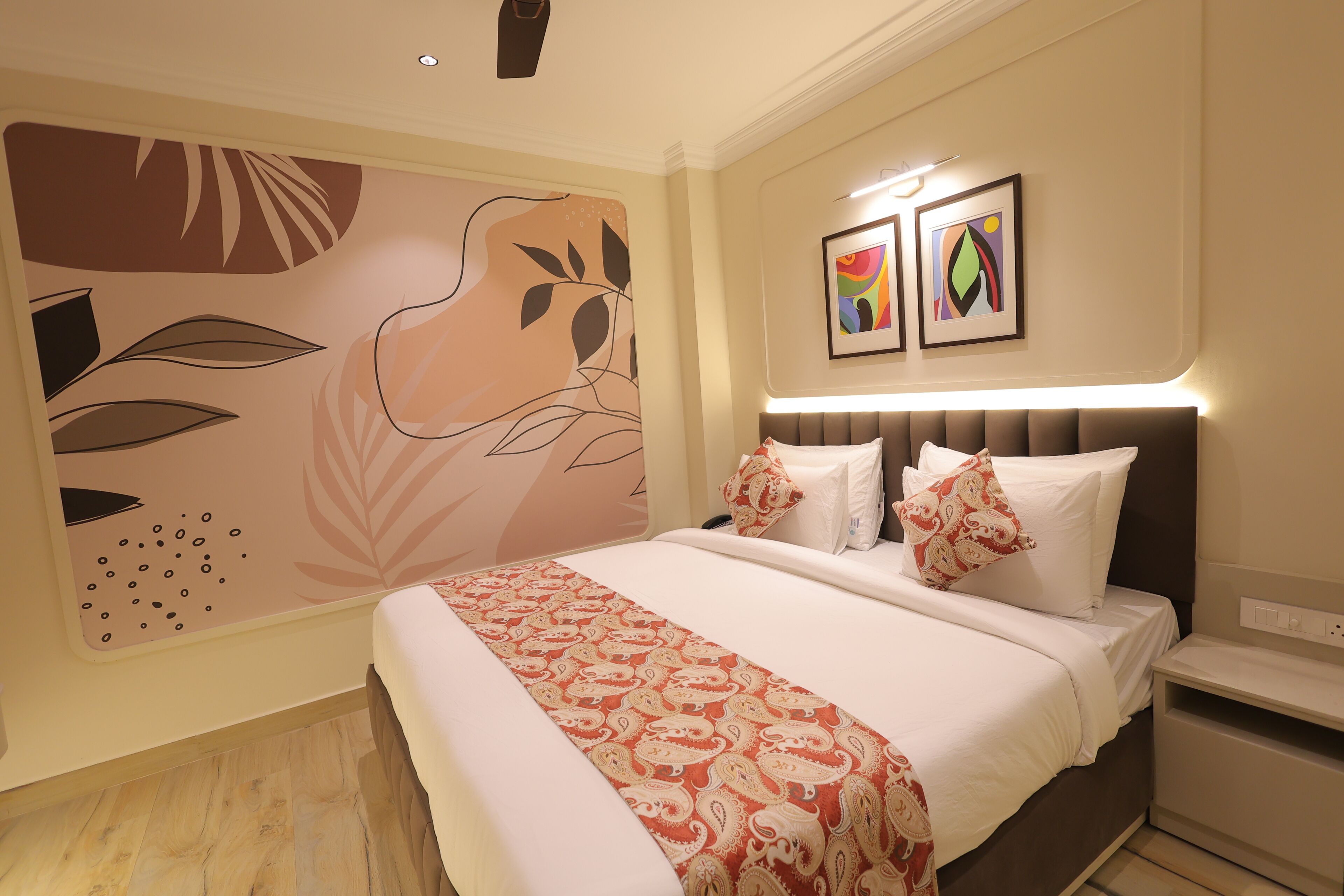 A hotel room with a large bed, a headboard with built-in lighting, a wall mural, and two framed artworks.