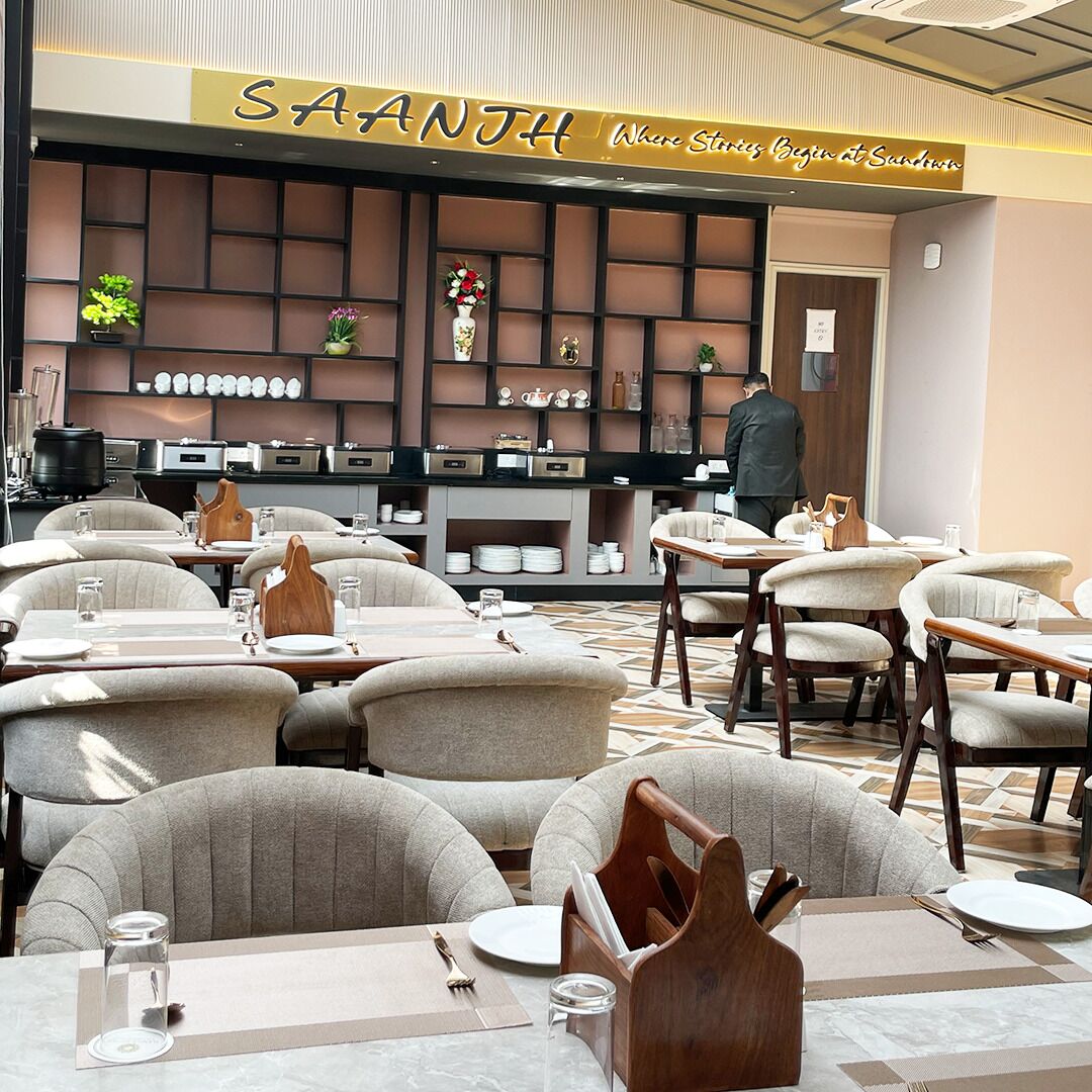 L’intérieur d’un restaurant présente un design moderne, avec un comptoir où figure le menu, un mur décoré de différents objets et plusieurs tables accompagnées de chaises.