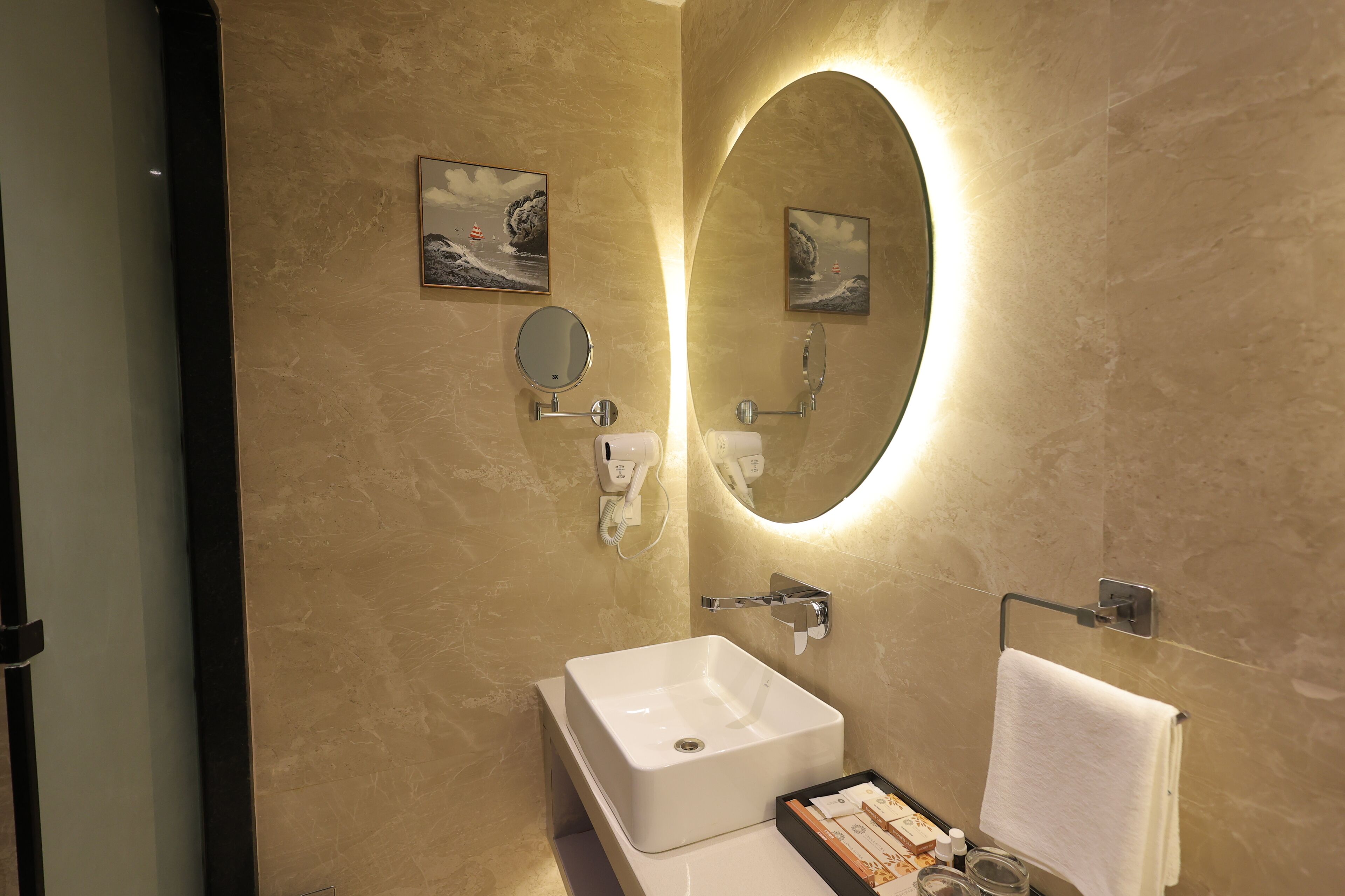 A modern bathroom with a large oval mirror, a white sink, and two framed pictures on the wall.