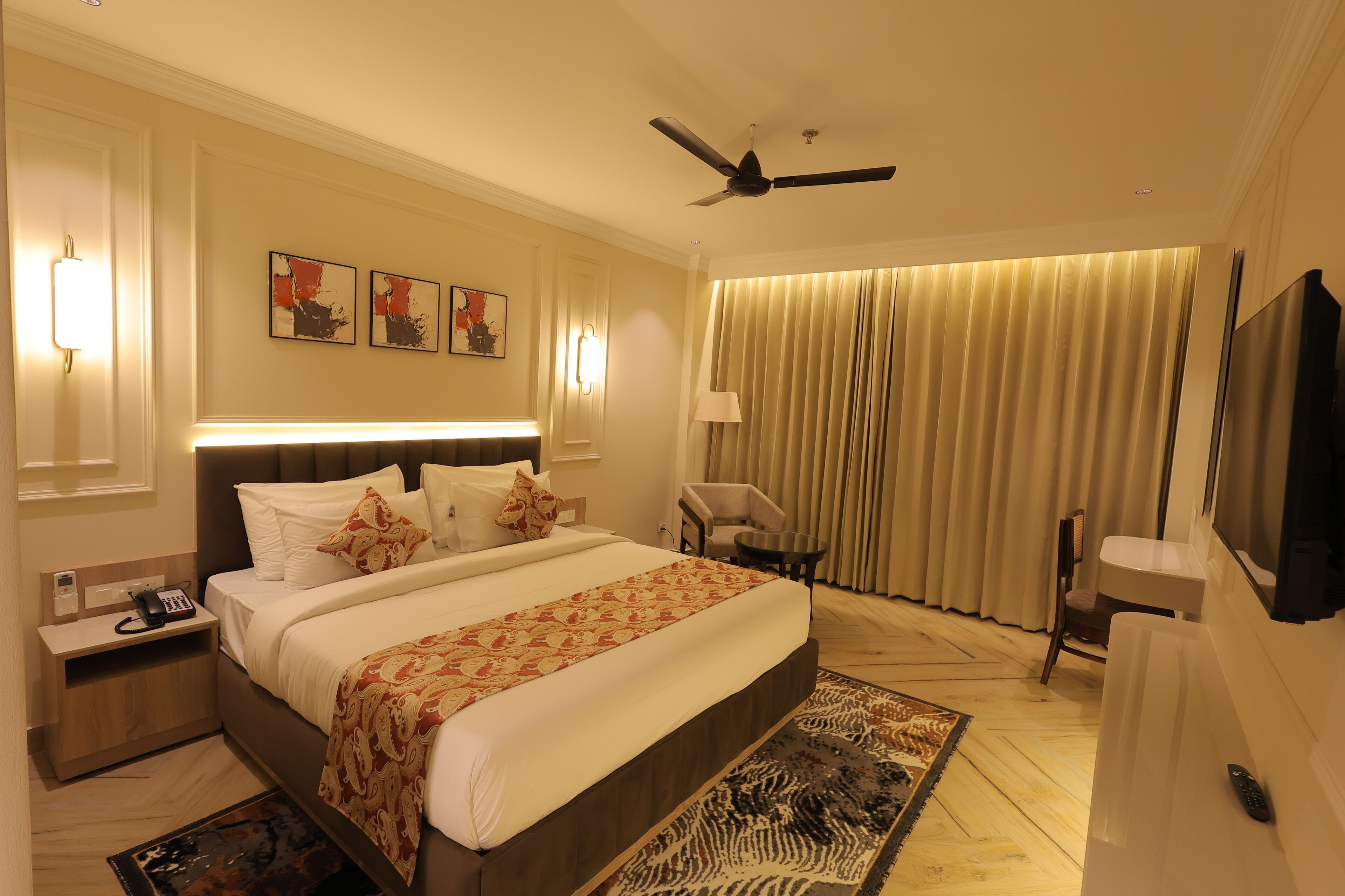 Ein Hotelzimmer mit einem großen Bett, Nachttischen, einem Schreibtisch, einem Sessel und einem Deckenventilator.