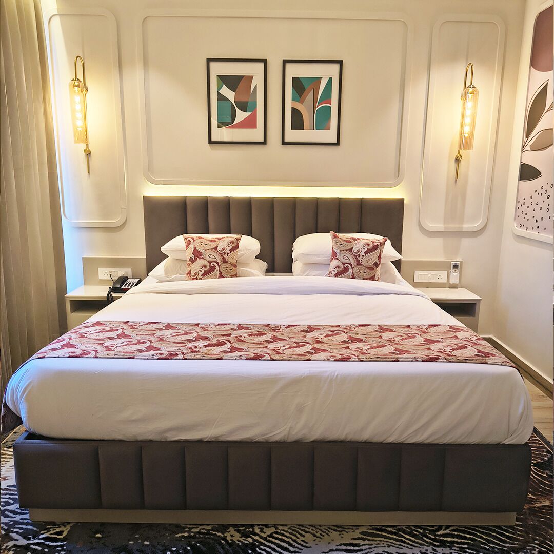 A hotel room with a large bed, two bedside tables, a nightstand, a telephone, and two wall-mounted light fixtures.