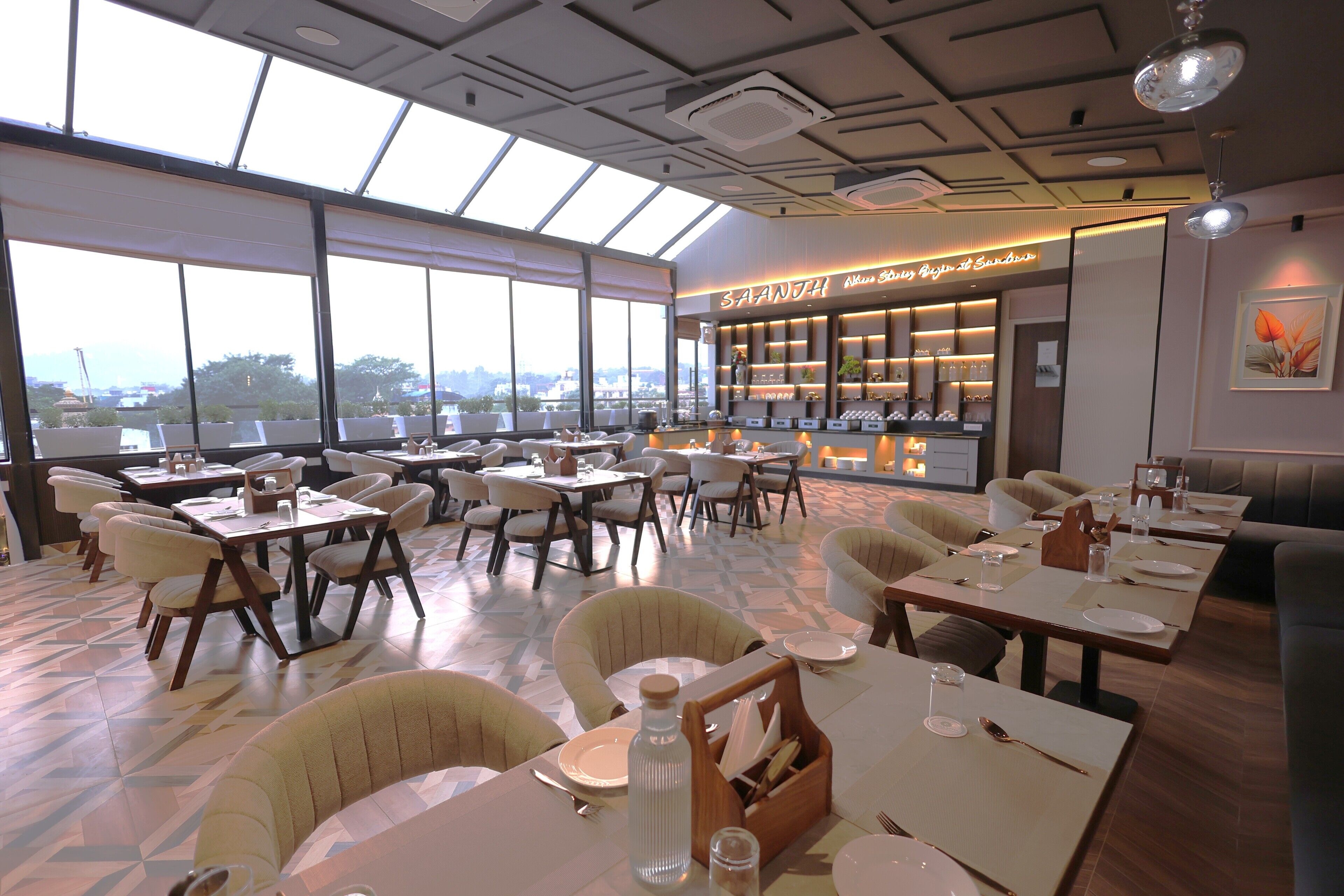 A restaurant with multiple dining tables and chairs, a bar area, and large windows offering a city view.