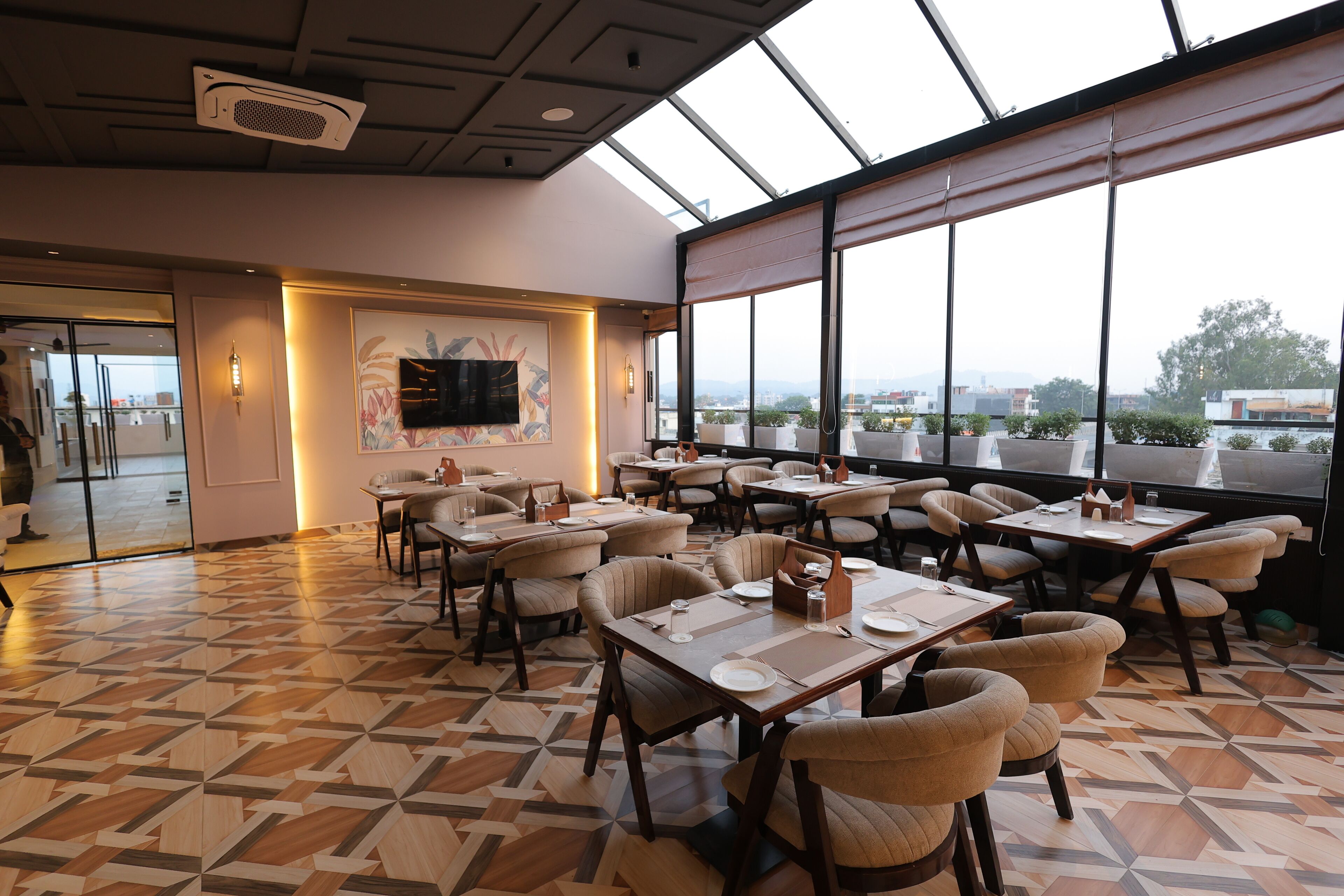 A restaurant with a geometric patterned floor, multiple tables with chairs, large windows offering a city view, and a modern ceiling design.